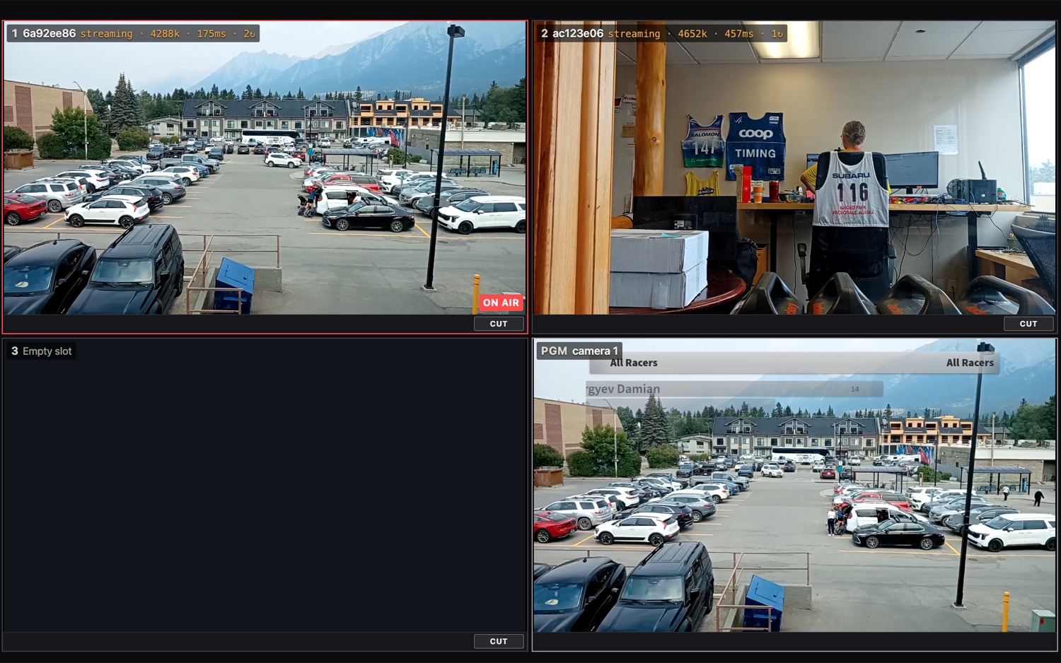 The multiview grid: camera 1 red-ringed and badged ON AIR showing a parking lot, camera 2 showing a timing room, an empty slot 3, and the PGM program tile carrying camera 1 with the racer-name overlay; each camera tile has a Cut button
